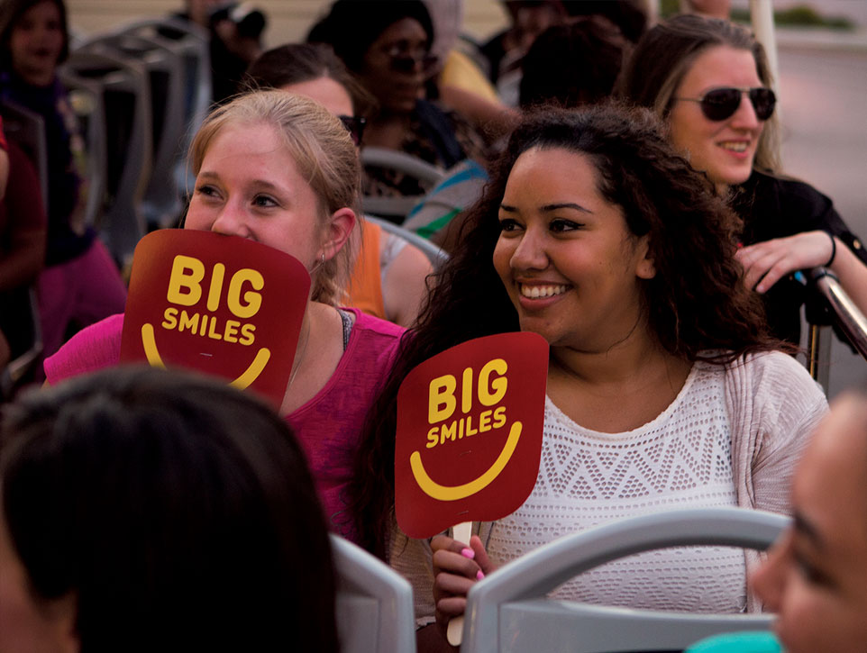 Two laides onboard a Big Bus holding branded signs
